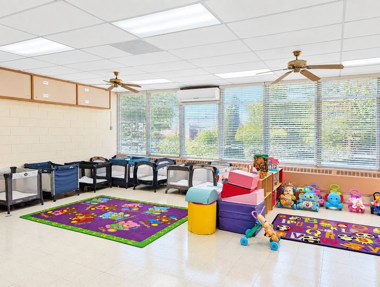Infant room with cribs, a colorful rug and soft play area