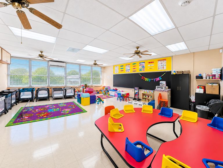 St. Luke's bright, organized infant classroom with cribs, a colorful rug and soft play area