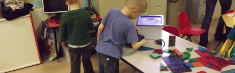 A child arranging colorful pattern blocks at a classroom table