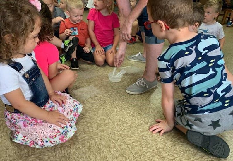 Children gathered on the floor around a teacher during a science activity